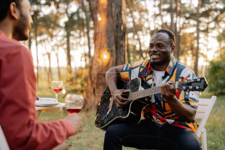 Foto de El hombre africano toca la guitarra para el indio que bebe vino y canta - Imagen libre de derechos