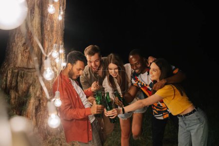 Foto de Una compañía de amigos multirraciales bebiendo cerveza en la fiesta, haciendo caras cerca de lámparas colgantes - Imagen libre de derechos