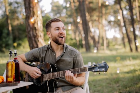 Photo for One bearded man is playing guitar. Summer holidays, vacation, relax and lifestyle consept. Camping time. - Royalty Free Image