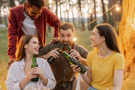 Foto de Amigos multirraciales divirtiéndose en una fiesta, chicos y chicas bromeando mientras abren cerveza con sus dientes - Imagen libre de derechos