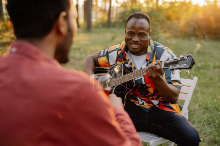 Foto de El hombre africano toca la guitarra para el indio que bebe vino y canta - Imagen libre de derechos