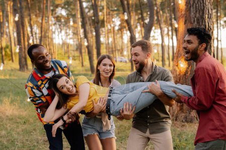 Téléchargez les photos : Groupe multiracial de personnes, d'amis jetant une fille dans les airs et s'amusant - en image libre de droit