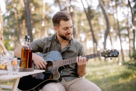 Photo for One bearded man is playing guitar. Summer holidays, vacation, relax and lifestyle consept. Camping time. - Royalty Free Image