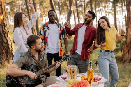 Téléchargez les photos : Groupe multiculturel de personnes, homme barbu hipster jouer de la guitare et des amis danser et s'amuser - en image libre de droit