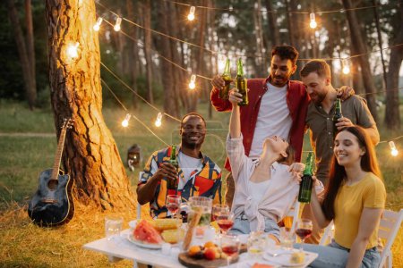 Foto de Grupo de amigos multirraciales divirtiéndose en la fiesta, bebiendo cerveza y haciendo tostadas - Imagen libre de derechos