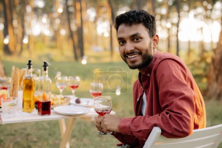 Foto de Retrato de hombre indio barbudo feliz bebiendo vino en el picnic con amigos - Imagen libre de derechos
