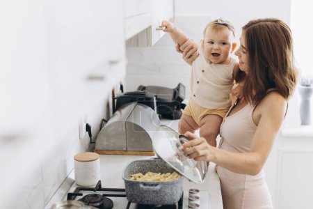 Photo for A mother with her little baby daughter prepares food in the kitchen - Royalty Free Image