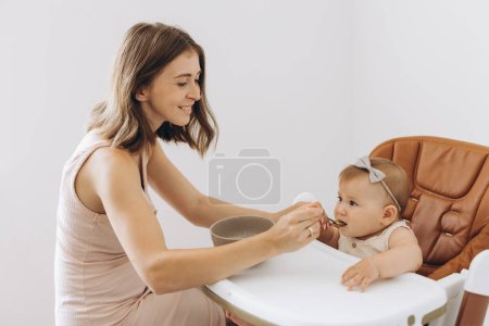 Photo for Mother feeding healthy food to her adorable little daughter sitting in high chair - Royalty Free Image