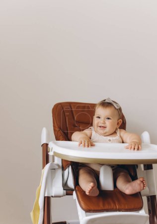 Téléchargez les photos : Joyeux bébé fille assis dans une chaise haute dans la cuisine à la maison - en image libre de droit