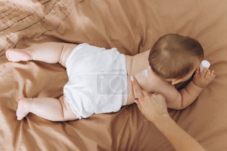 Téléchargez les photos : Mère heureuse appliquant de la crème sur le corps de sa petite fille - en image libre de droit