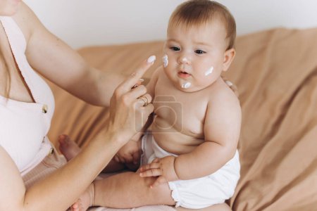 Feliz madre aplicando crema en el cuerpo y la cara de su bebé