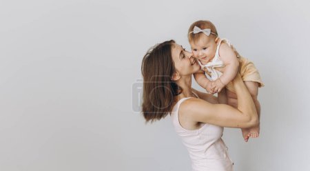 Téléchargez les photos : Mère heureuse avec son adorable bébé fille tout en soulevant dans les airs sur fond blanc - en image libre de droit