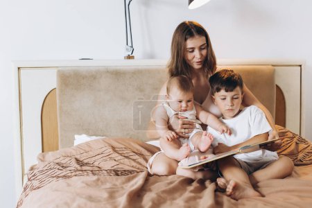 Photo for A young mother reads a fairy tale to her children, a boy and a little baby girl - Royalty Free Image