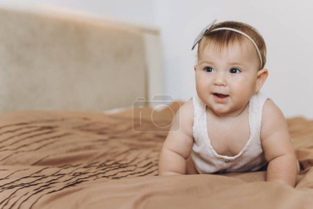 Téléchargez les photos : Portrait d'une petite fille souriante et rampante sur le lit dans la chambre - en image libre de droit