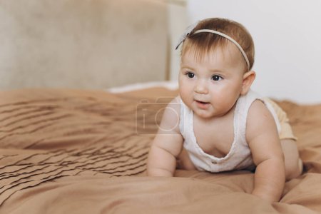 Téléchargez les photos : Portrait d'une petite fille souriante et rampante sur le lit dans la chambre - en image libre de droit