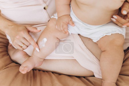 Téléchargez les photos : Mère heureuse appliquant de la crème sur le corps de sa petite fille - en image libre de droit