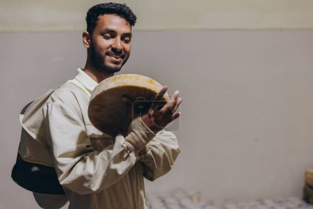Photo for Portrait of happy young Indian beekeeper holding wax and honey and working in beekeeping factory - Royalty Free Image