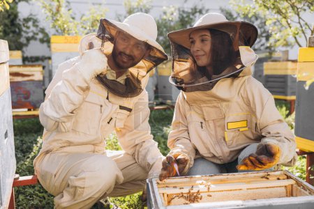 Foto de Un par de felices apicultores sonrientes trabajando con herramientas apícolas cerca de la colmena en la granja de abejas - Imagen libre de derechos