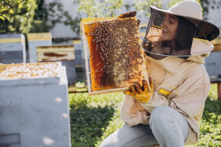 Joyeux souriant femme apiculteur en costume de protection tenant cadre abeille avec des abeilles au rucher