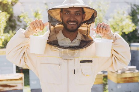 Téléchargez les photos : Joyeux apiculteur indien souriant tenant prêt miel biologique fabriqué dans une ferme apicole - en image libre de droit