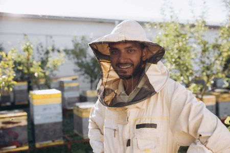 Téléchargez les photos : Portrait d'un heureux apiculteur indien travaillant dans un rucher près d'une ruche avec des abeilles. Ramasse du miel. Apiculteur sur rucher. Concept apicole. - en image libre de droit