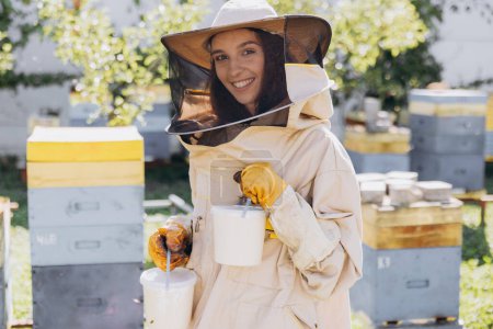 Téléchargez les photos : Joyeux souriant apiculteur femelle tenant prêt miel biologique fabriqué dans la ferme apicole - en image libre de droit