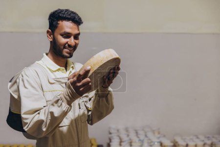 Foto de Retrato de un joven apicultor indio feliz sosteniendo cera y miel y trabajando en una fábrica de apicultura - Imagen libre de derechos
