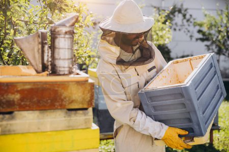 Téléchargez les photos : Apiculteur déplace une ruche dans le jardin d'une ferme apicole, concept apicole - en image libre de droit