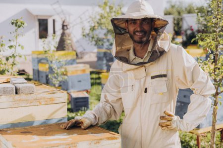 Téléchargez les photos : Portrait d'un heureux apiculteur indien travaillant dans un rucher près des ruches avec des abeilles - en image libre de droit