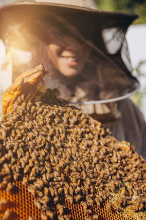 Téléchargez les photos : Gros plan Apiculteur femelle en costume de protection tenant un cadre d'abeilles avec des abeilles au rucher - en image libre de droit