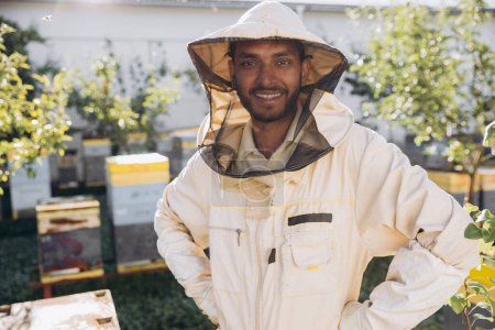 Photo for Portrait of a happy Indian male beekeeper working in an apiary near beehives with bees. Collect honey. Beekeeper on apiary. Beekeeping concept. - Royalty Free Image