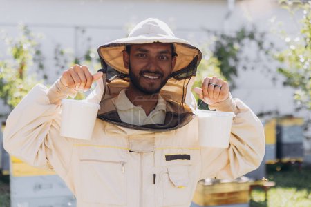 Téléchargez les photos : Joyeux apiculteur indien souriant tenant prêt miel biologique fabriqué dans une ferme apicole - en image libre de droit
