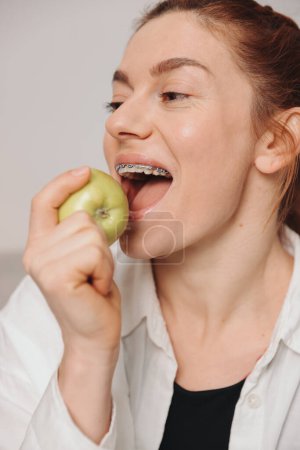 Photo for Portrait of mature woman with braces on teeth eating green apple - Royalty Free Image