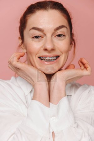 Foto de Mujer feliz moderna mostrando sonrisa con tirantes sobre fondo rosa - Imagen libre de derechos