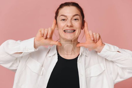 Foto de Mujer feliz moderna mostrando tirantes sobre fondo rosa, concepto de ortodoncia - Imagen libre de derechos