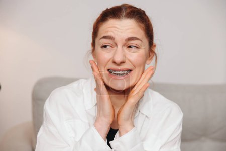 Téléchargez les photos : Portrait d'une femme mûre aux cheveux roux souffrant de douleur due à un appareil dentaire - en image libre de droit