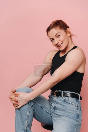 Téléchargez les photos : Femme musclée sportive en t-shirt et jeans riant émotionnellement avec bretelles sur fond rose - en image libre de droit
