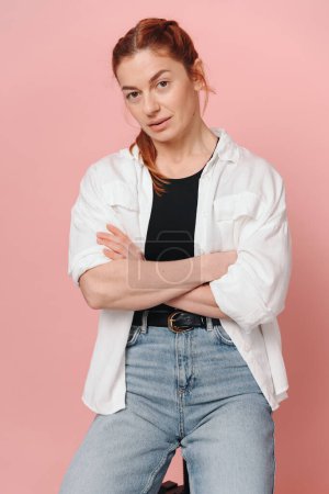 Photo for Modern sporty woman with red hair wearing shirt and jeans posing on pink background - Royalty Free Image