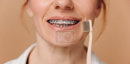 Foto de Acercamiento femenino en tirantes sosteniendo un cepillo de dientes sobre un fondo beige - Imagen libre de derechos