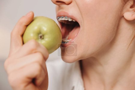 Téléchargez les photos : Portrait de femme mature avec bretelles sur les dents mangeant de la pomme verte - en image libre de droit