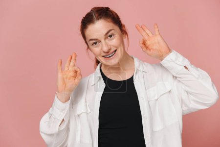 Photo for Modern happy woman showing braces on pink background, orthodontics concept - Royalty Free Image