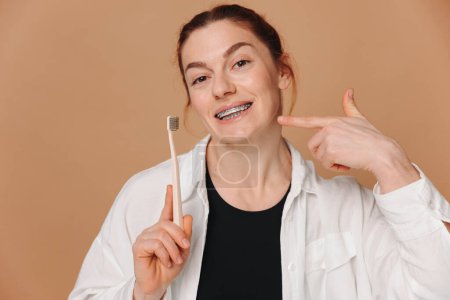 Photo for Happy mature woman in braces holding a toothbrush on a beige background - Royalty Free Image