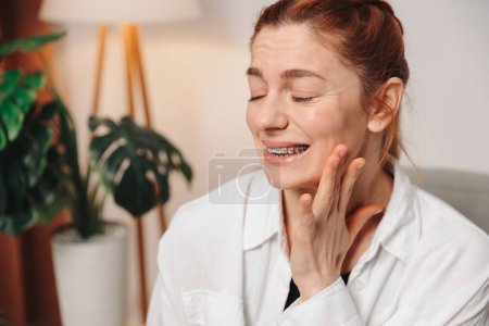 Photo for Portrait of red-haired mature woman suffering from pain due to braces - Royalty Free Image