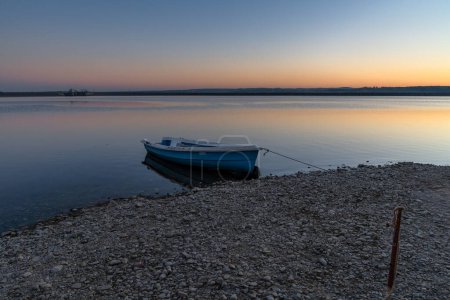 Téléchargez les photos : Beau coucher de soleil sur le lac Budeasa dans le centre de la Roumanie avec une barque en bois attachée sur la plage rocheuse - en image libre de droit