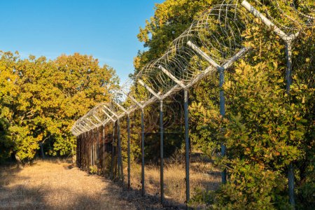 Blick auf einen hohen Zaun mit Stacheldraht, der durch den Wald an der Grenze zwischen der Türkei und Bulgarien führt