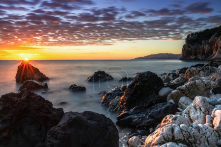 Téléchargez les photos : Un lever de soleil coloré à Cala Gonone avec des roches noires et blanches et des rochers au premier plan - en image libre de droit