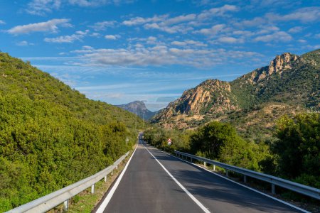 Téléchargez les photos : Autoroute asphaltée menant à travers les montagnes verdoyantes centrales de la Sardaigne sous un ciel bleu - en image libre de droit