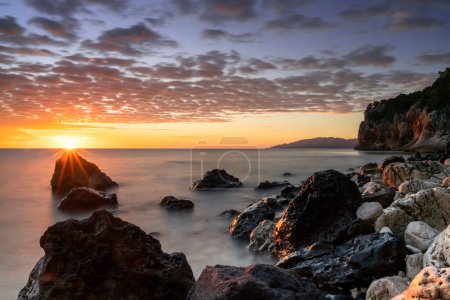 Téléchargez les photos : Un lever de soleil coloré à Cala Gonone avec des roches et des rochers noirs et blancs et un coup de soleil - en image libre de droit