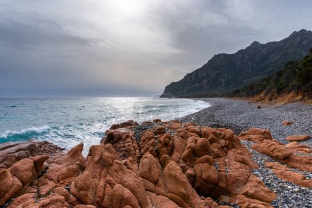 Téléchargez les photos : Côte sauvage et accidentée en Sardaigne avec des vagues s'écrasant sur la plage rocheuse et des rochers de granit rouge au premier plan - en image libre de droit