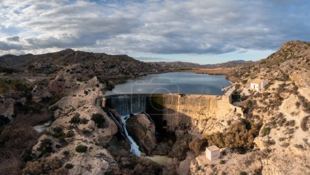 A drone view of the Elche Reservoir and dam wall with waterfall and surrounding semi-desert landscape